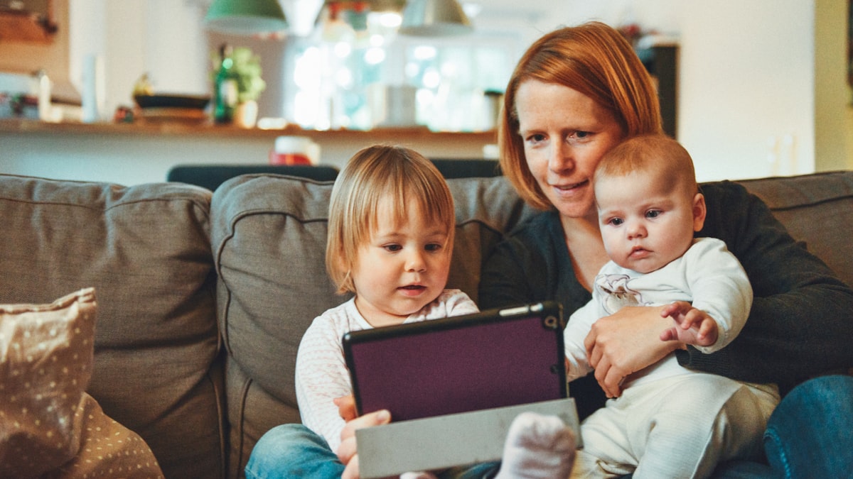 Mama si copii pe canapea uitandu-se impreuna la o tableta